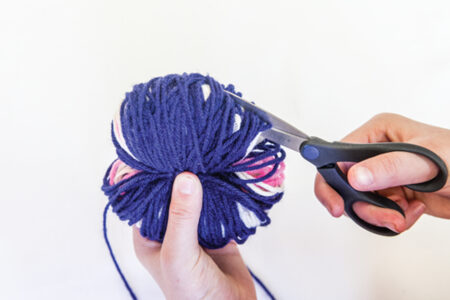 person using scissors to cut in to a wound ball of yarn